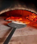 9 Inch Round Perforated Aluminum Pizza Peel With Detachable 40 Inch Handle Lightweight Yet Durable Pizza Turner For High Heat Ovens Outdoor Pizza Oven Accessories For Easy Slide And Turn Pro Grade, shown sliding pizza in oven.
