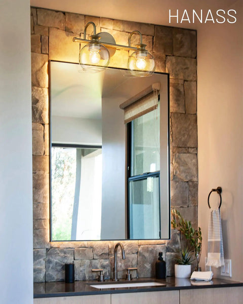 Gold Finish 15 Inch Two Light Vanity Light With Clear Globe Glass Shades over bathroom mirror on stone wall
