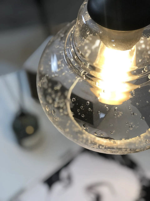 Close-up of 8 Inch Seeded Bubble Glass Pendant Light Fixture With Hand Blown Shade, glowing bulb inside, oil rubbed bronze finish.