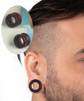 Close-up of person wearing Three Pairs Organic Wood Ear Plugs Set With Double Flared Ear Tunnels Saddle Fit Wooden Gauges Five Eighths Inch 16mm Natural Black Brown Tones Perfect For Punk Piercing And Everyday Wear