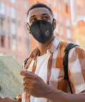 Person wearing NIOSH Approved N95 Face Masks for Adults, 30 Pack, Five Layer Filtration, outdoors with backpack and map