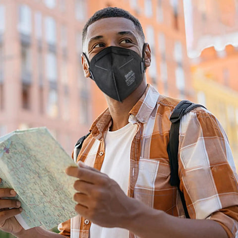Person wearing NIOSH Approved N95 Face Masks for Adults, 30 Pack, Five Layer Filtration, outdoors with backpack and map