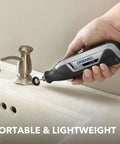 Dremel Lite cordless rotary tool held in hand beside a sink, gray/black body with a small grinding wheel attached.