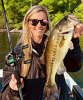 Person holding bass with Torrent Lite Ultra Light Baitcasting Reel With Carbon Body, 5.5 Oz Lightweight Build, on a sunny day.