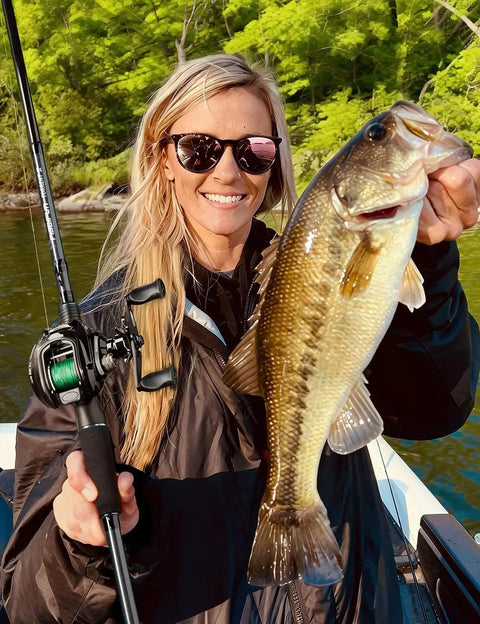 Person holding bass with Torrent Lite Ultra Light Baitcasting Reel With Carbon Body, 5.5 Oz Lightweight Build, on a sunny day.