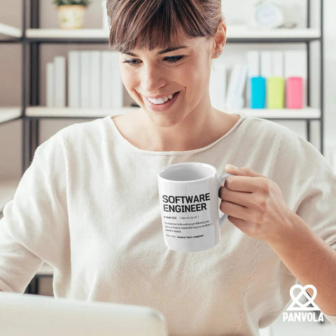 Woman holding Engineer Definition Mug A Nerdy Yet Real Talk Engineering Gift For Engineers Graduation Birthday Or Promotion Celebrations Perfect Ceramic Mug 11 Oz White For Coworkers And New Engineers, smiling while working on a laptop.