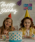 Happy Birthday Neon Sign Dimmable LED Light For Backdrops And Party Decor above kids in birthday hats with polka dot cake.
