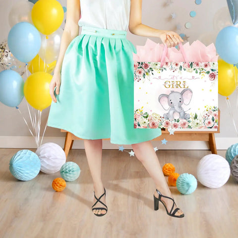 Woman holding a 13 Inch Large Baby Shower Gift Bag For Girls With Pink Floral Elephant Design And Durable Handles Includes Tissue Paper Pack And Greeting Card No Fuss Quick Gift Wrapping For Baby Showers Or Birthday Parties, surrounded by decorative balloons.