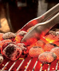 Close-up of heated coals in the Original Kettle Premium Charcoal Grill 22 Inch Black Outdoor BBQ Grill with tongs.