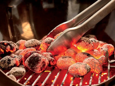Close-up of heated coals in the Original Kettle Premium Charcoal Grill 22 Inch Black Outdoor BBQ Grill with tongs.