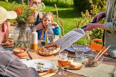 Heavy Duty 14 Inch Bamboo Pizza Peel And Wooden Spatula Paddle For Backyard Cookouts, serving pizza outdoors.