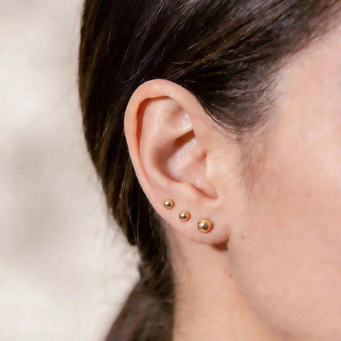 Five Piece Gold Ball Stud Earrings Set For Women Including 3mm 4mm 5mm 6mm And 7mm Sizes, 14K Gold Plated With 316L Steel Pins, Super Versatile Everyday Earrings. Three gold ball studs on ear