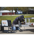 Welder using Auto-Darkening Welding Helmet With Three Independent Arc Sensors in outdoor setting, kneeled beside metal structure