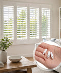 100 Count White Spring Loaded Shutter Pins Quick Snap Hardware For Plantation Window Shades shown in a home setting with a hand holding clips.
