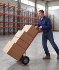 Man using Heavy Duty Metal Hand Truck With 600 Pound Capacity And Ergonomic P Handle, shuffling boxes in a warehouse.