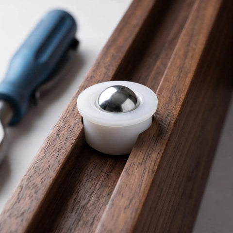 Close-up of 12pcs Steel Ball Transfer Casters with Nylon Housing, 0.7x0.5in, installed in wooden track with tool.