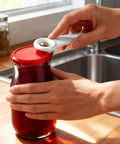 Person using 6 Pack Jar Lid Opener Tool Set Featuring Long Lever Handle to pop a vacuum seal on a glass jar.
