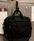 Black laptop bag hanging on 4 Pack Adjustable Cubicle Hooks For 1.8 To 3.5 Inch Panels And Walls, Plastic Coat Hooks.