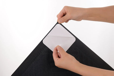 Hands applying Rug Gripper Set Of 4 Non Slip Corner Pads For Hardwood Floors And Tile, Reusable Washable Double Sided Adhesive Stickers