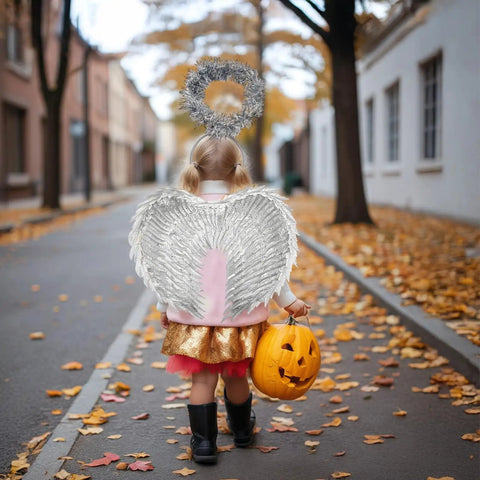 Child wearing Girls Silver Angel Wings With Headband Set for Halloween Costume, holding a pumpkin bucket on a leaf-covered street.