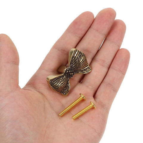 Copper Bowknot Cabinet Handle And Drawer Pull Kit In Vintage Brass Finish held in hand with screws for installation