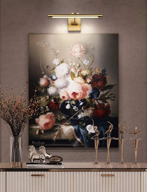 Dimmable LED Picture Light With Swing Arm, 16.5 Inch Dope Brass Finish Wall Lamp illuminating floral artwork in hallway.