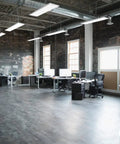 Modern office space with desks and computers under exposed ductwork ceiling with hanging lights.