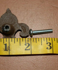 Old School Vintage Fleur De Lis Cabinet Knob next to yellow measuring tape, cast iron, Victorian style, with screw.