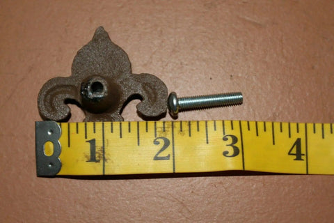 Old School Vintage Fleur De Lis Cabinet Knob next to yellow measuring tape, cast iron, Victorian style, with screw.