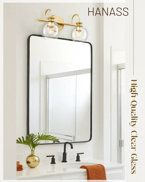 Gold Finish 15 Inch Two Light Vanity Light With Clear Globe Glass Shades above a mirror in a modern bathroom setting