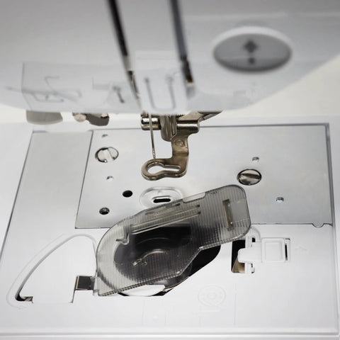 Bobbin cover plate area on a sewing machine; front view shows exposed bobbin housing, metal needle plate, and clear presser foot.