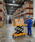 Warehouse scene with Beast Mode 350 lb Hydraulic Lift Table Cart with Double Scissor Lift, loaded with boxes.