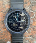 Analog-digital wristwatch with black rubber strap, displaying time, date, and health metrics, against a textured stone surface.