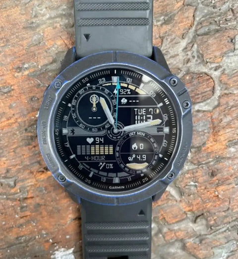 Analog-digital wristwatch with black rubber strap, displaying time, date, and health metrics, against a textured stone surface.