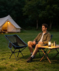 Ultralight Folding Camp Chair For Backpacking And Hiking Fourth Gen Compact And Lightweight Easy Setup Sturdy Steel Frame And Oxford Fabric Mesh Black Includes Carry Bag For Beach Camp Picnic And Mountaineering in outdoor setting with tent and person seated.