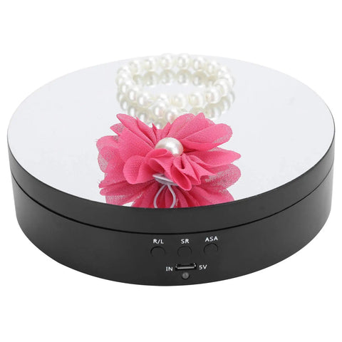 Upgrade Your Game With This Sick Electric Rotating Display Stand Boasting 3 Speeds And 4 Adjustable Angles For Showcasing Jewelry Watches And Cosmetics Like A Boss On A Sleek Black Mirror Surface Turntable Base with pink flower and pearl bracelet.