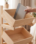 Top Notch Solid Wood Two Tier Floor Storage Rack With Slanted Tray Bins In Warm Brown Finish Zero Hassle Minimalist Design For No Sweat Home Organization And Clutter Free Spaces with a hand placing a book in a slanted tray.