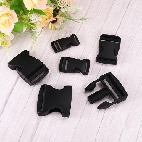 2 Pack 1-1/2 Inch Side Release Buckles in black displayed on wood surface with floral decoration, suitable for backpacks and luggage.