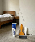 Easy Diy Drywall Repair Paste For Quick Fixes That Seals Cracks And Holes Tile Grout And Concrete Shower Floor Waterproof Sealant Wall Mending Paste Tube with tools next to a cracked wall in a room.
