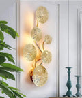 Lux Lotus Leaf Wall Sconce Night Light With Gold Finish on a white wall near decor items and plants