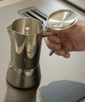 Hella Durable Stainless Steel Stovetop Espresso Maker For Rich Coffee Brews with open lid, held in hand, showing smooth finish.
