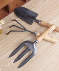 Three Kinds Of Gardening Tools Set Featuring Hooked Mattock Hand Shovel And Trident For Everyday Garden Work And Shoreline Shell Collecting On Tide Flats Built With Iron Heads And Wooden Handles In A Durable Black Finish, displayed on wooden surface