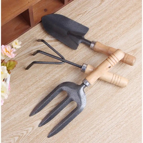 Three Kinds Of Gardening Tools Set Featuring Hooked Mattock Hand Shovel And Trident For Everyday Garden Work And Shoreline Shell Collecting On Tide Flats Built With Iron Heads And Wooden Handles In A Durable Black Finish, displayed on wooden surface