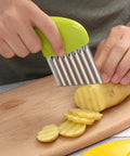 Green-handled stainless steel crinkle cutter slicing potatoes on a wooden cutting board