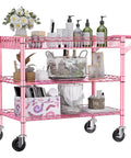 Rock Solid Heavy Duty Pink Metal Rolling Cart With Three Roomy Shelves And Smooth Rolling Wheels filled with beauty products and decor.