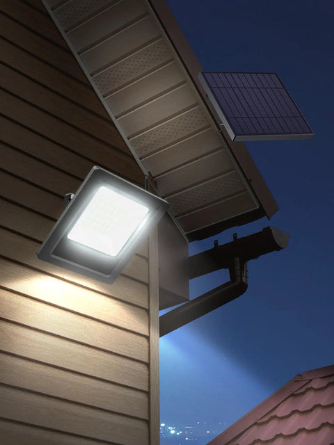 Outdoor Solar Flood Light 6500K Cool White Dope Bright Light mounted under eave with solar panel, illuminating yard at night.
