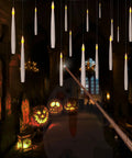 Flameless Taper Floating Candles With Magic Wand Remote 20 Piece Set Dope Flickering Warm Light Battery Operated Six Inch LED Window Candles For Christmas Weddings Halloween And Birthday Party Decor hanging in a dark room with lit pumpkins at a Halloween party.