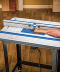 High Pressure Laminate Router Table Top With 10 Point Plate Leveling For Precision Cuts Smooth Low Friction Routing Surface MDF Core Woodworking Table Top Pro Fence Compatible With Adapter Kit Sold Separately, showing a hand guiding a wooden board along the fence for precise cutting.