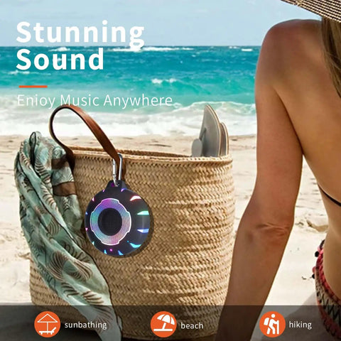 Waterproof Shower Bluetooth Speaker With IPX7 Rating hangs from a beach bag, showing carabiner and LED lights beside person on beach.