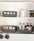 Two bamboo storage racks with jars and bottles on white shelves in kitchen cabinet, mugs hanging below